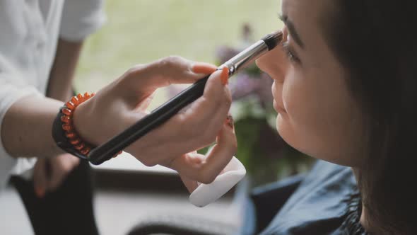 Hand of Makeup Artist Makes Makeup on Face of Beautiful Young Woman Using Makeup Brush