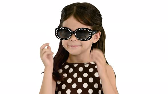 Darkhaired Little Girl in Polkadot Dress Putting on Black Sun Glasses and Waiving To the Camera on