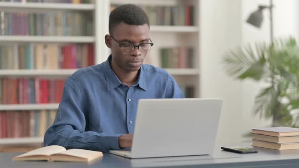 Young African Man Looking at Camera While Using Laptop