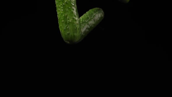 Three Juicy Cucumbers Fly Up Spinning and Fall on a Black Background in Slow Motion Shot