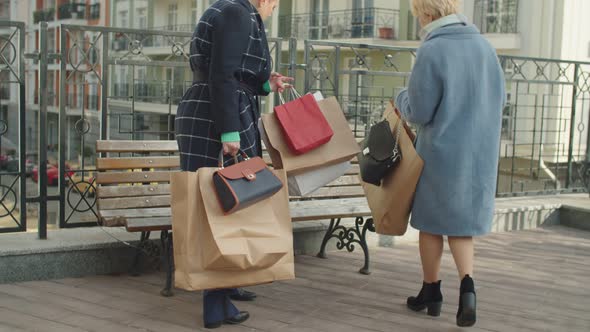 Elderly Female Buyers with Many Paper Bags Rubbing Sore Feet Outdoors