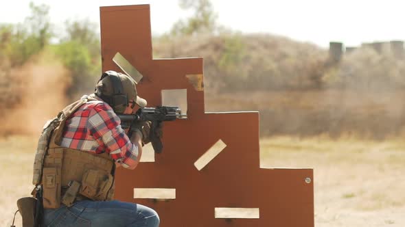 Caucasian Man in Headphones Sunglasses Firing Airsoft Gun Sitting Behind Cover Position