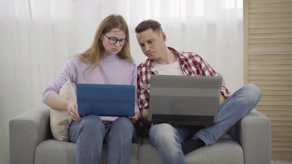 Young Redhead Millennial Woman in Eyeglasses Asking Boyfriend for Help with Laptop