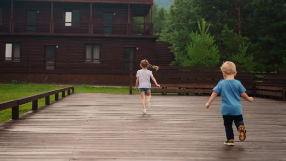 Little Boy Chases Sister Running Along Wooden Dance Deck