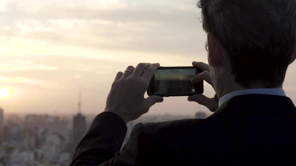 Rear view of businessman taking picture of city with smartphone