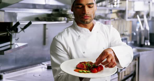 Male chef holding food plate in commercial kitchen