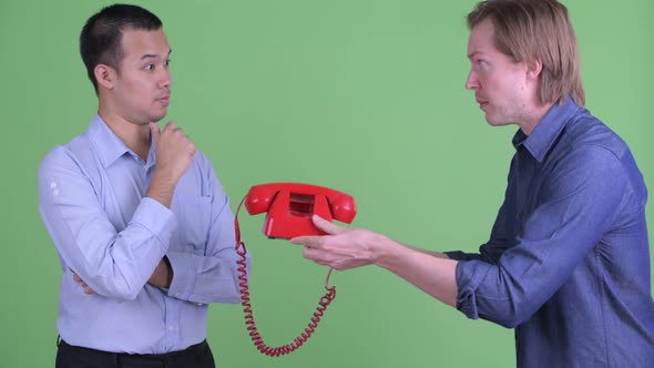 Young Businessman Giving Telephone To Stressed Asian Businessman Looking Angry