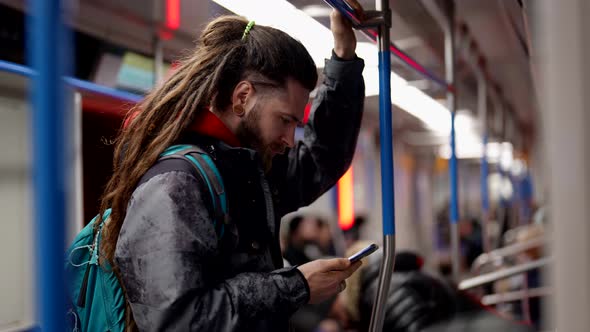 A Handsome Bearded Man Standing in Public Transport is Typing Text Messages on a Mobile Phone