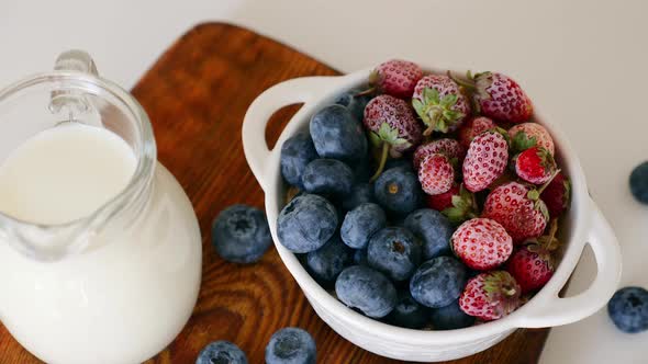 Breakfast Cup with Ripe Blueberries and Strawberries Jug with Milk on the Table