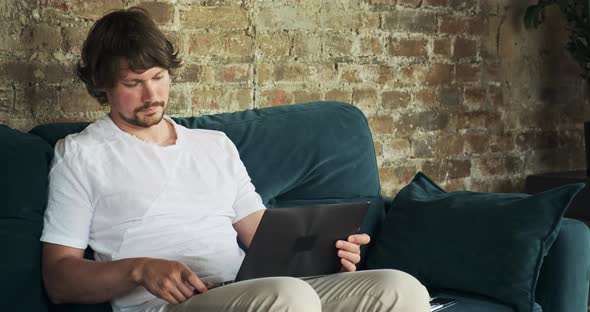 A Freelancer Works Remotely From Home on a Laptop Sitting on the Couch