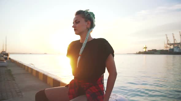 Young Stylish Funky Girl with Green Hair Riding Roller Skates and Dancing Near Sea Port During