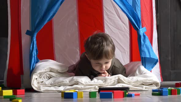 Little toddler boy in house watching cartoons on mobile phone at home