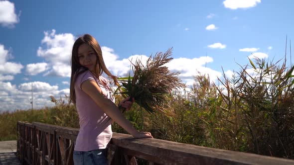 Happy Nice Fun Girl in Pink T-shirt Look in Camera with Reed in Her Hand. Then Hide From Camera