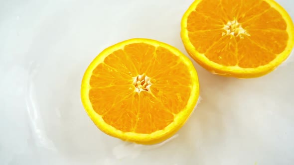 Rotating segments of a ripe and juicy orange in water on an white background. Slow motion.