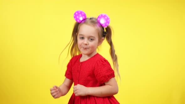 Cute Cheerful Girl in Red Dress and Toy Mouse Ears Dancing in Slow Motion at Yellow Background