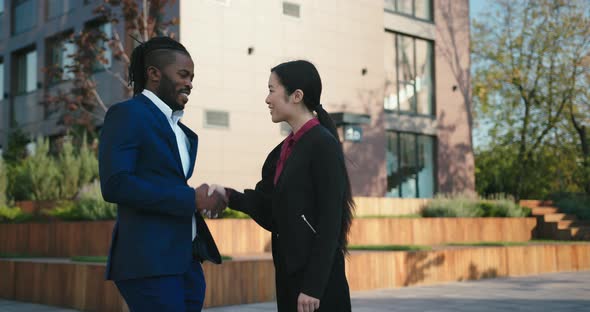 Asian Woman Shakes Black Man Hand Against Office Building