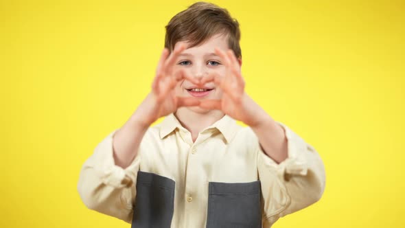 Positive Caucasian Boy Making Heart Shape with Hands Looking at Camera Smiling