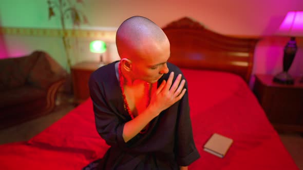 Medium Shot of Young Sad Transgender Sitting on Bed in Red Light Thinking