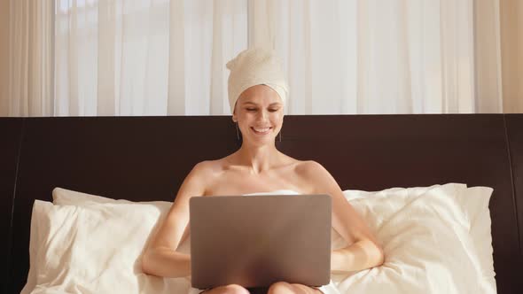 Smiling Young Woman Sitting on Bed Using Laptop Notebook Looking at Screen