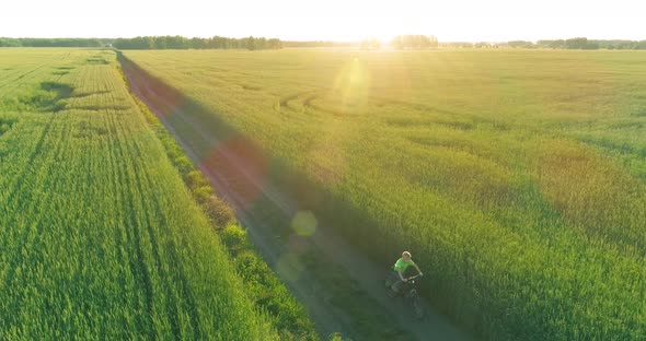 Aerial View on Young Boy That Rides a Bicycle Thru a Wheat Grass Field on the Old Rural Road