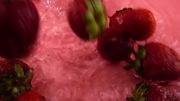 Falling strawberries into the water on a pink background. Slow motion.