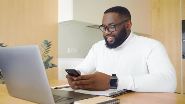 African American Businessman Freelancer Using Smartphone and Laptop at Home