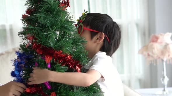 Asian Child Hanging Decorative Toy Together On Christmas Tree