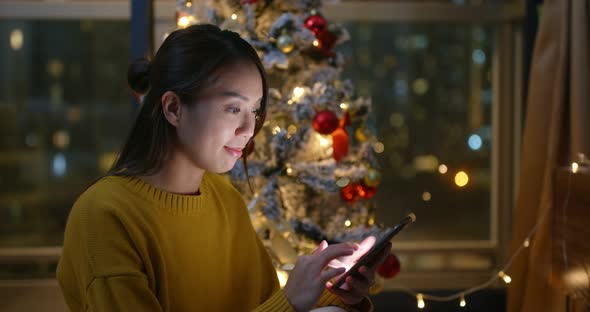 Woman use of smart phone with christmas tree decoration at home in the evening