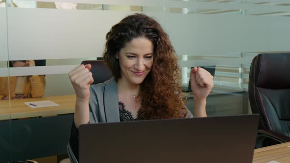 Happy woman feeling excited looking at laptop screen sitting at workplace being promoted.