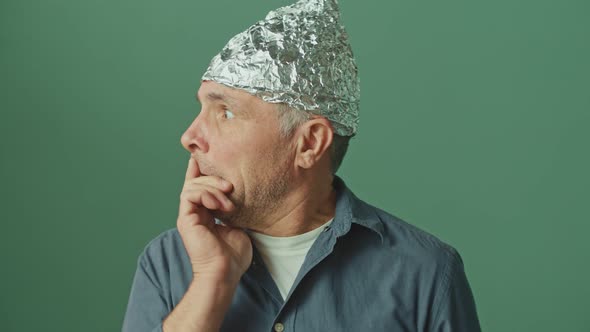 A Paranoid Man with a Protective Foil Cap on His Head Looks Around Anxiously