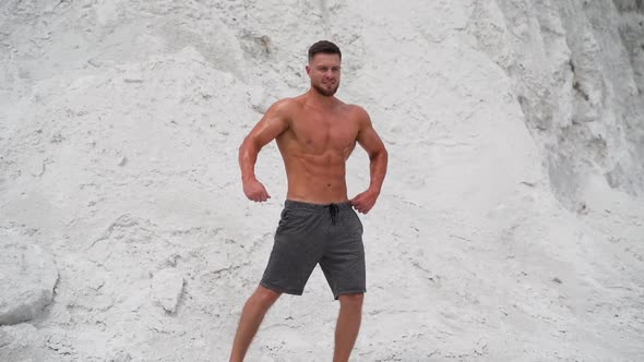 Shirtless man in shorts shows his muscles outdoors.