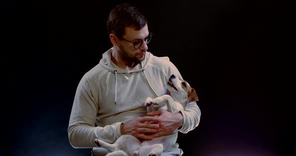 Handsome Man Is Sitting with Jack Russell Dog in Hands in Dark Room