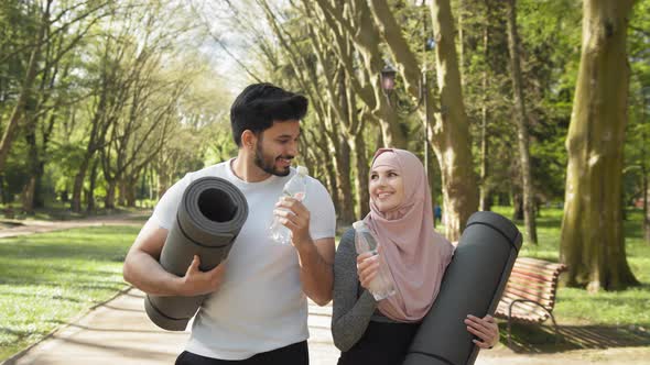 Happy Muslim Woman and Man Toasting with Bottle of Fresh Water After Training at