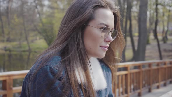 Portrait of Young Glamour Woman in Jeans Jacket Standing on the Wooden Bridge Looking Around and in