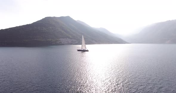 White Sailboat Floats on the Sea Against the Background of Mountains in the Fog