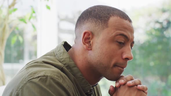 Portrait of thoughtful biracial man sitting on sofa and turning around