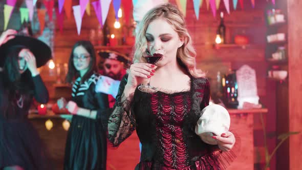 Vampiress Fulfills Her Taste of Blood at a Halloween Party with a Skull in Her Hands