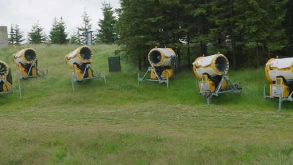 Snow Dispensers Stand on Green Hill Slope on Cloudy Day