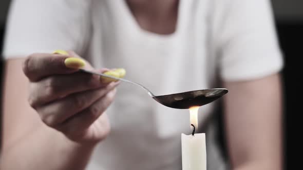 Young Woman Drug Addict Cooking Drugs in Spoon on Candle Flame