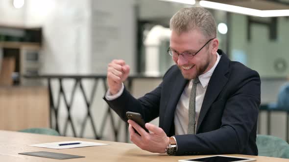 Businessman Celebrating Success on Smartphone in Office