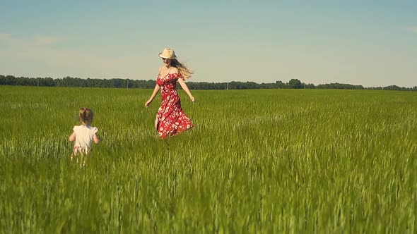 Slow Motion Young Mother Plays with Child in the Field Dressed in Red Dress That Flutters in the