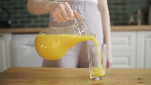 Close Up of Woman Pouring Orange Juice Into the Glass From Jar on Kitchen in Morning