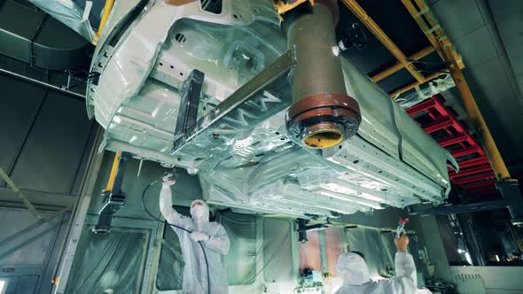 Two Factory Workers Painting a Car Body From Below