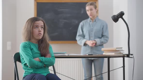 Portrait of Young Stubborn Little Woman with Crossed Hands Rolling Eyes As Blurred Teacher Talking