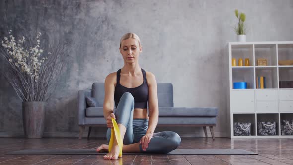 Young and sporty girl in sportswear is doing exercises in home interior using resistance band.