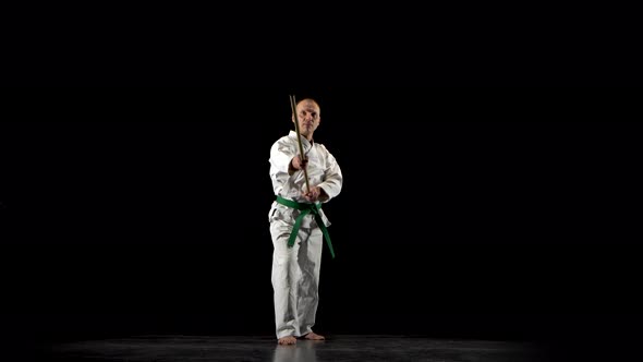 Kendo Fighter on White Kimono Practicing Martial Art with the Bamboo Bokken on Black Background.