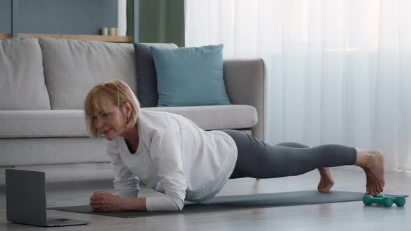 Older Lady Exercising At Laptop Standing In Plank At Home