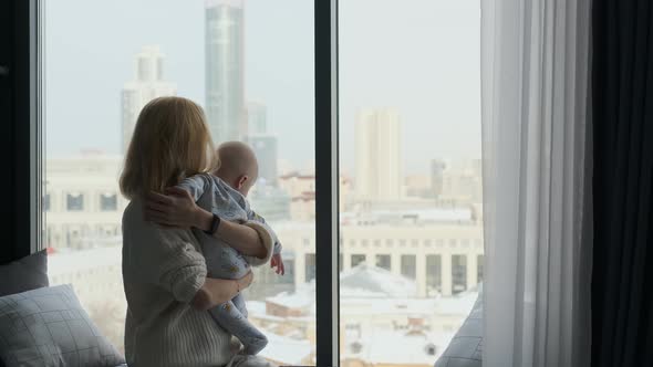 mom with son in her arms look out the window at the city