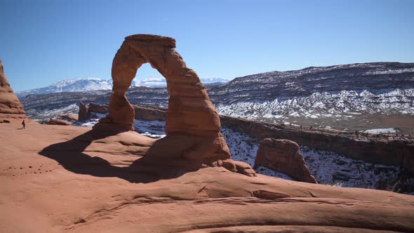 Hiker walking up to and climbing on the Delicate Arch in Arches National Park, pan