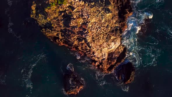 Rising aerial view of rocky cliffs and foaming ocean waves at sunset in Big Sur California